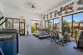 A gym with treadmills, elliptical machines and a fan.